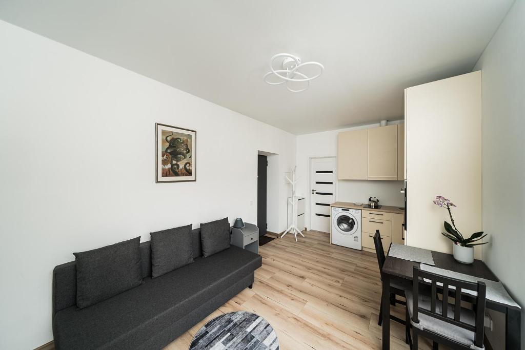 a living room with a black couch and a kitchen at Zalgirio Arena Apartment No1 by URBAN RENT in Kaunas