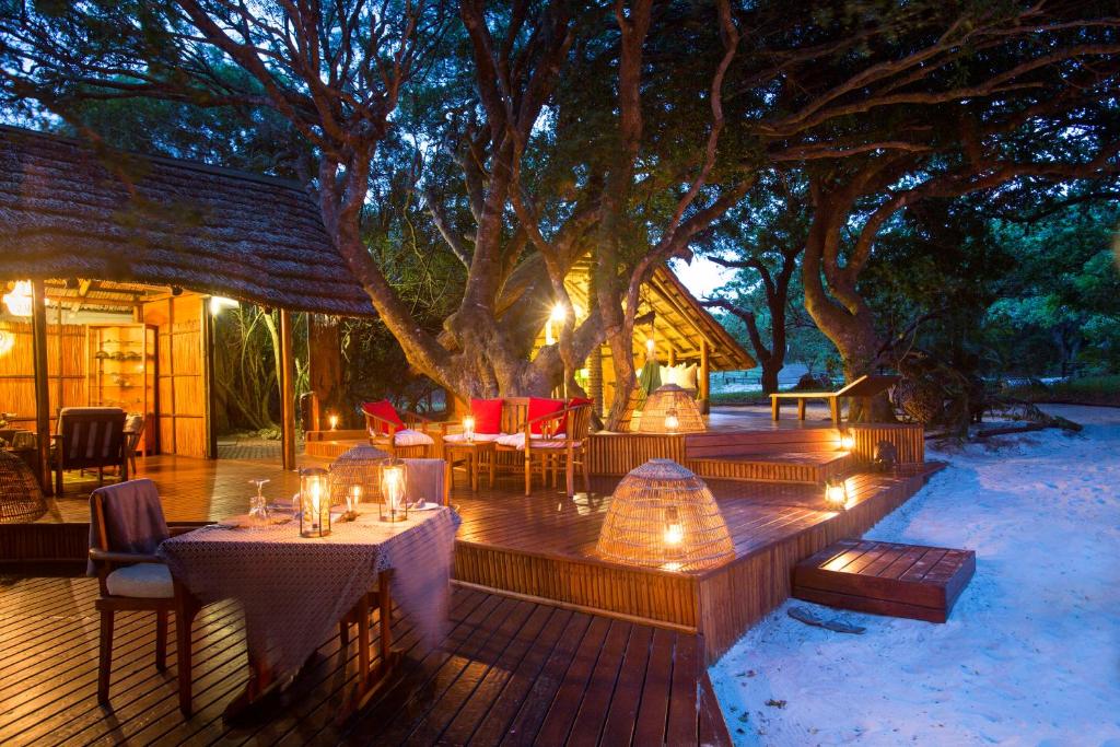 eine Holzterrasse mit Tischen und Stühlen unter einem Baum in der Unterkunft Kosi Forest Lodge in Manguzi