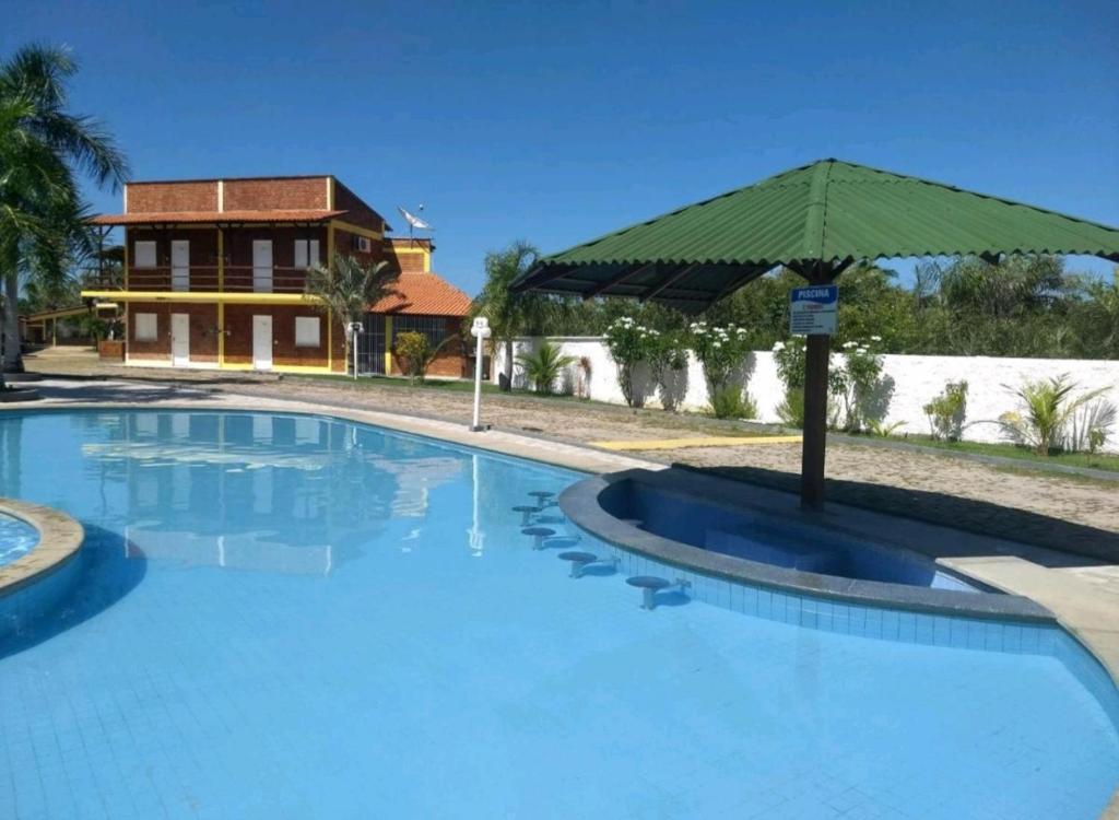 a large swimming pool with an umbrella in front of a house at Chalé Descanso in Barreirinhas