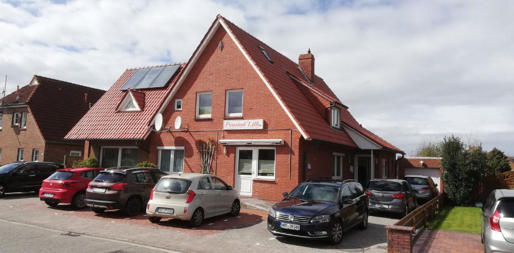 een rood bakstenen huis met auto's geparkeerd op een parkeerplaats bij Pension Lilli in Norddeich
