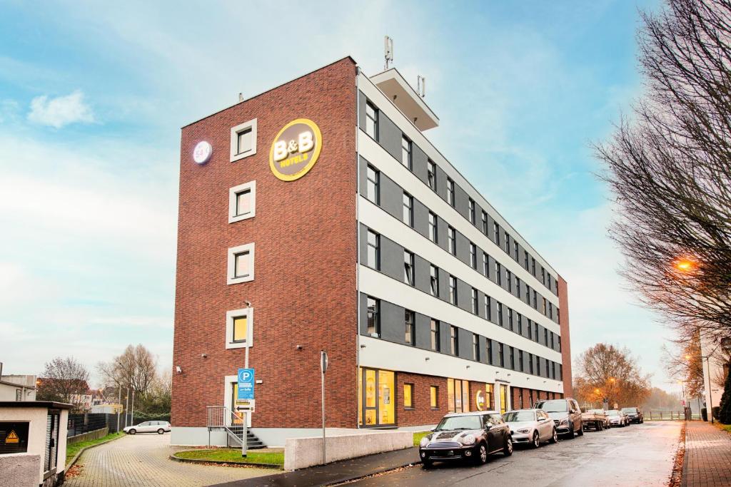 een groot bakstenen gebouw met auto's geparkeerd voor het bij B&B Hotel Kassel-City in Kassel