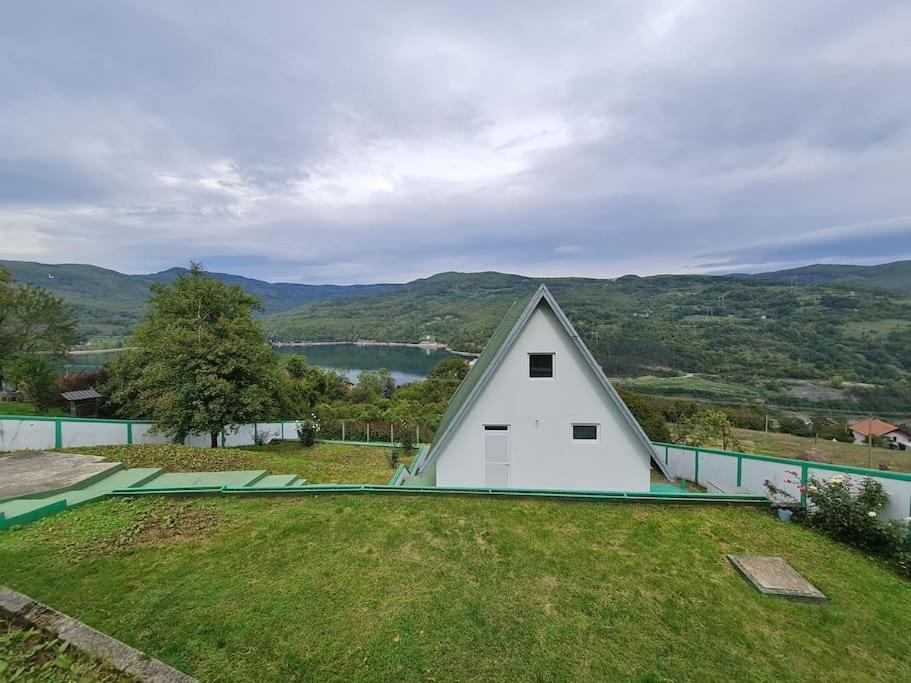 une petite maison blanche au-dessus d'un champ verdoyant dans l'établissement Green House with Lake View, à Perućac
