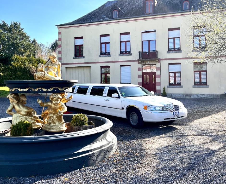 ein weißes Auto, das vor einem Gebäude mit einem Brunnen parkt in der Unterkunft Domaine des anges in Avesnes-sur-Helpe