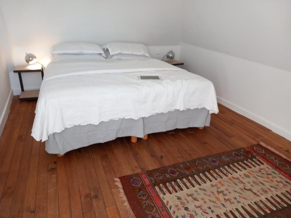 um quarto com uma cama com lençóis brancos e um tapete em Gîte "Chez elles" à Arnac-Pompadour em Arnac-Pompadour