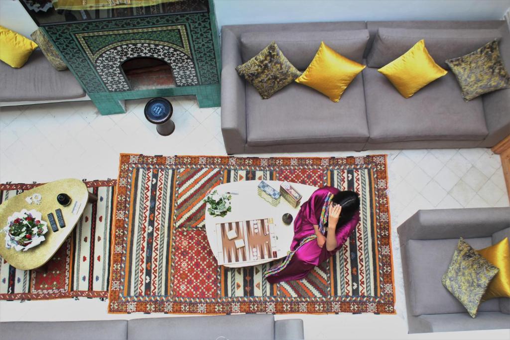 RIAD LUXE LOCATION le GRIZZLY في مراكش: امرأة تجلس على سجادة على أريكة