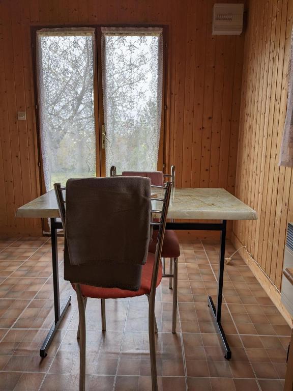 a table and chairs in a room with two windows at Au petit chalet d&#39;Illiers Combray in Illiers