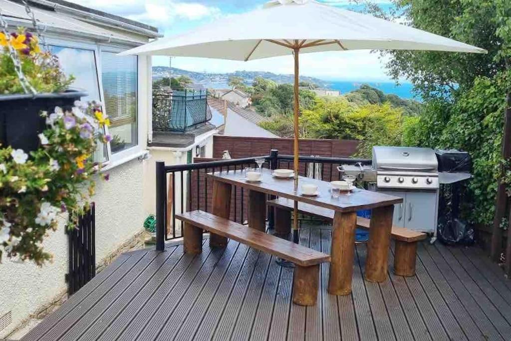 una terraza de madera con mesa de picnic y sombrilla en 3 Bedroom Bungalow with great Sea Views, Private Hot Tub & Gardens, en Paignton
