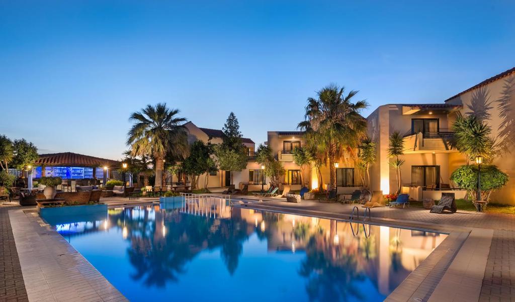 a swimming pool with palm trees and buildings at Nireas Hotel in Kato Daratso