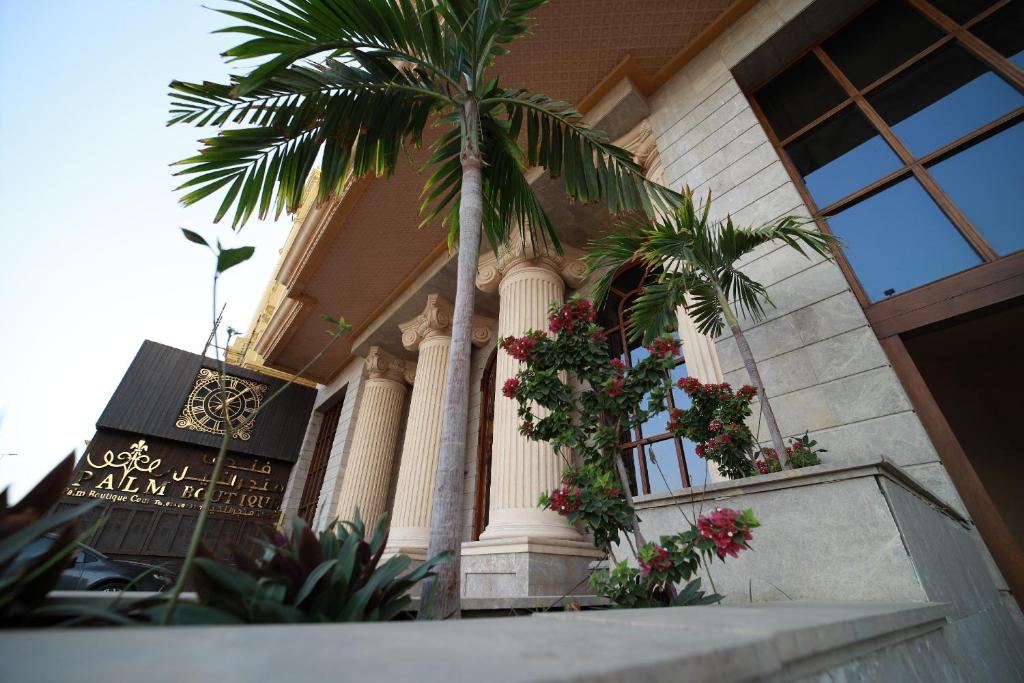a palm tree in front of a building with flowers at Palm Boutique Hotel in Jeddah