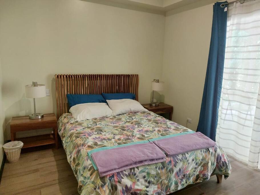 1 dormitorio con 1 cama, 2 mesitas de noche y ventana en Condo Playa Hermosa, Puntarenas, en Muñeco