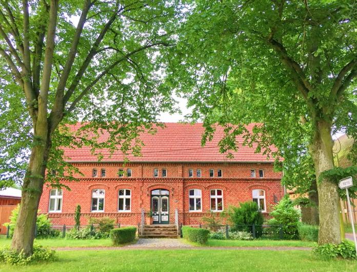um grande edifício de tijolos vermelhos com árvores em frente em Romantische Ferienwohnung Unter den Linden em Buchholz