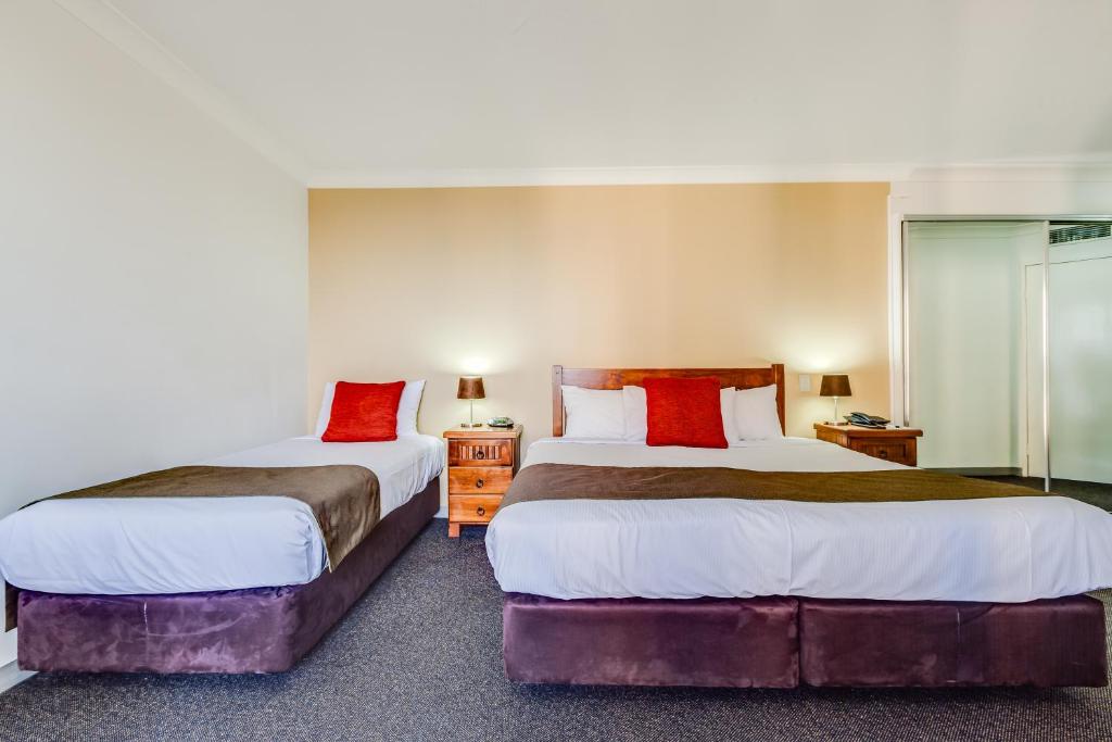 Dos camas en una habitación de hotel con almohadas rojas. en Hillcrest Apartment Hotel (formerly Central Hillcrest Apartments), en Brisbane