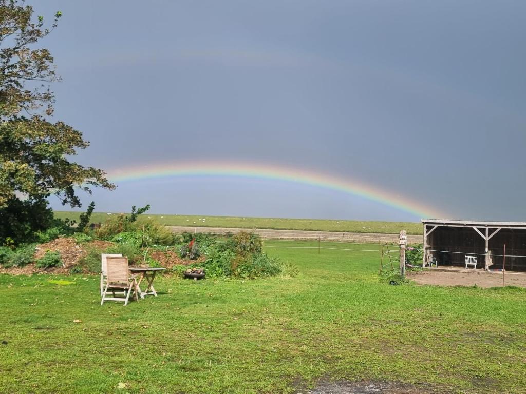 un arco iris sobre un campo con una mesa y una silla en Ferienwohnungen Das Finkhaus, en Simonsberg