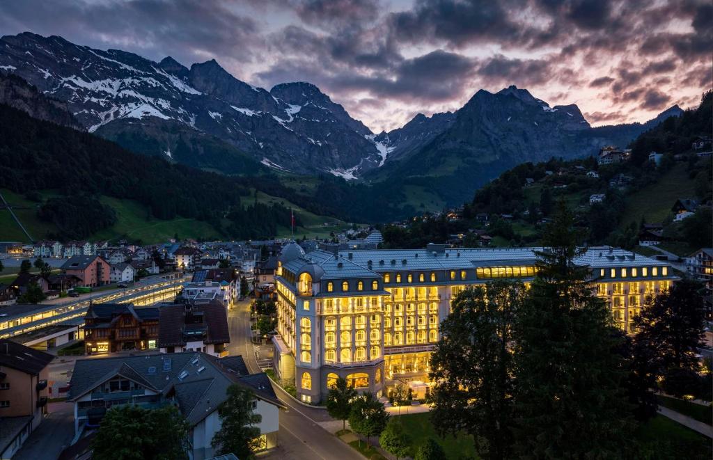 a building lit up at night with mountains in the background at Kempinski Palace Engelberg in Engelberg