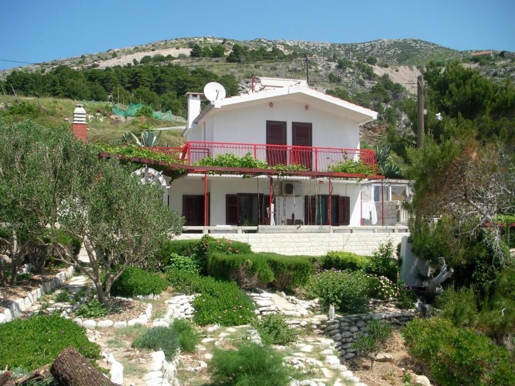 a white house with a red balcony on a hill at Apartments by the sea Cove Zarace, Hvar - 21007 in Hvar