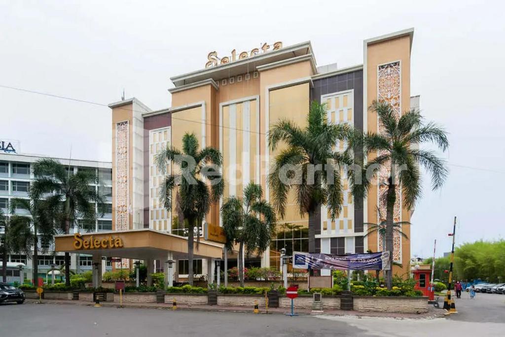 un gran edificio con palmeras delante en Selecta Hotel Medan Petisah R Signature Mitra RedDoorz, en Medan