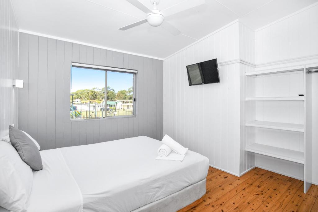 a white bedroom with a bed and a window at Lakeside Cabins & Holiday Village in Sussex inlet