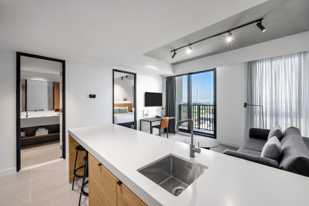 an apartment kitchen with a sink and a living room at Nesuto Docklands in Melbourne
