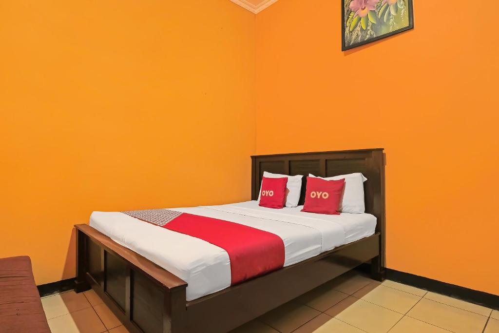 a bedroom with a bed with orange walls and red pillows at OYO 92486 Hotel Permata 3 in Salatiga
