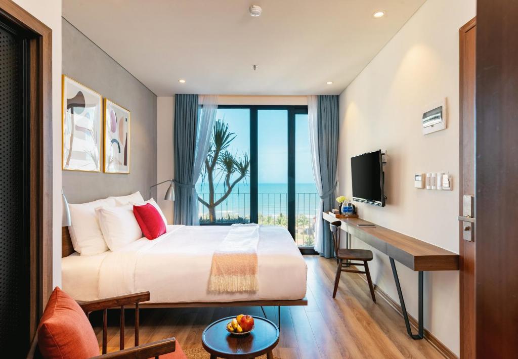 a bedroom with a bed and a desk with a television at The Glomad Danang Hotel in Da Nang