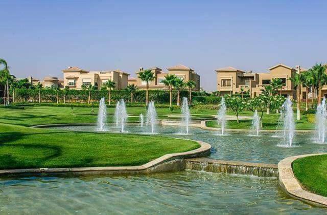 a fountain in a park in front of some houses at مدينتى in Madinaty