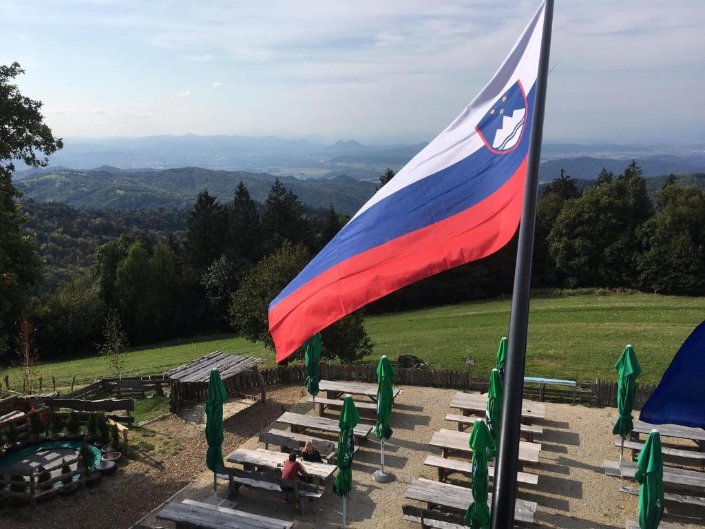 uma bandeira num mastro de bandeira com bancos e mesas em Planinski dom Janče em Ljubljana