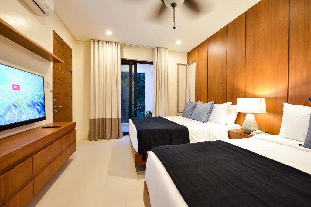 a hotel room with two beds and a flat screen tv at The Apartments at El Nido in El Nido