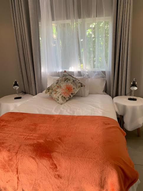 a bed with an orange blanket and a window at KLOOFIES GUESTHOUSE in Roodepoort