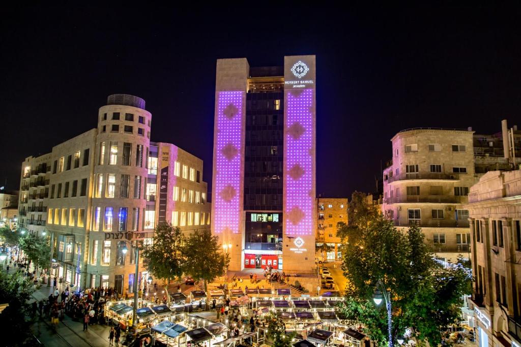 een hoog gebouw met paarse lichten er 's nachts op bij Herbert Samuel Jerusalem in Jeruzalem