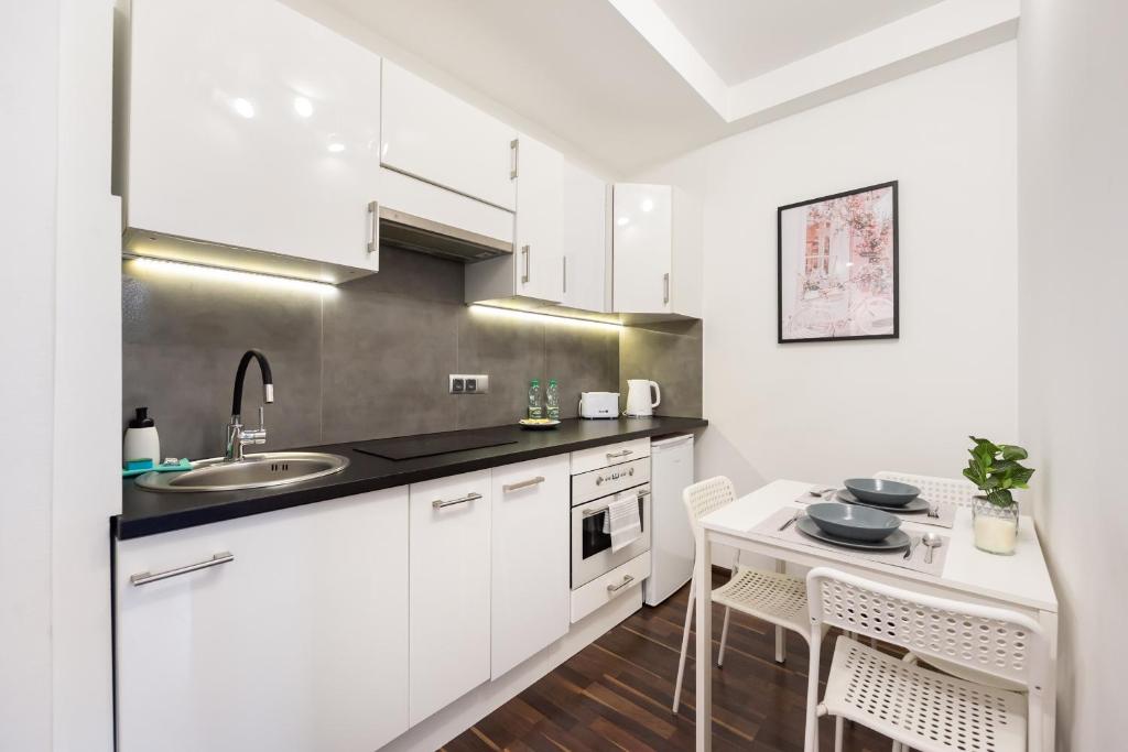a kitchen with white cabinets and a sink and a table at Dobra Old Town Apartment in Warsaw