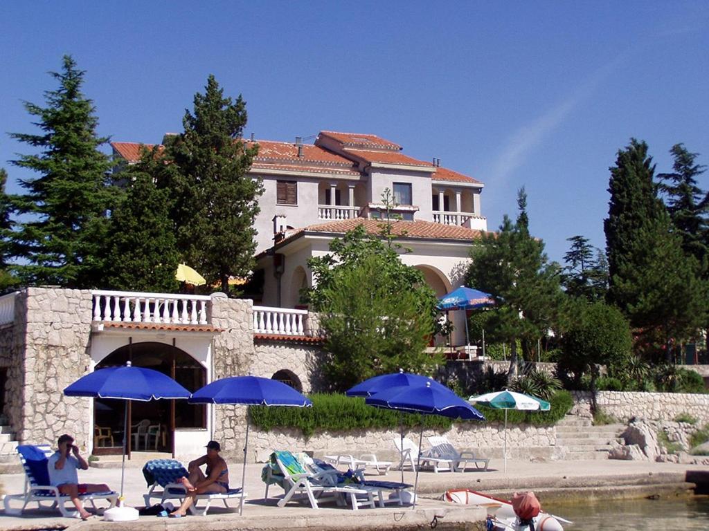 a group of people sitting under umbrellas in front of a house at PENSION SEA QUEEN JADRANKA DIREKT am MEHR in Omišalj