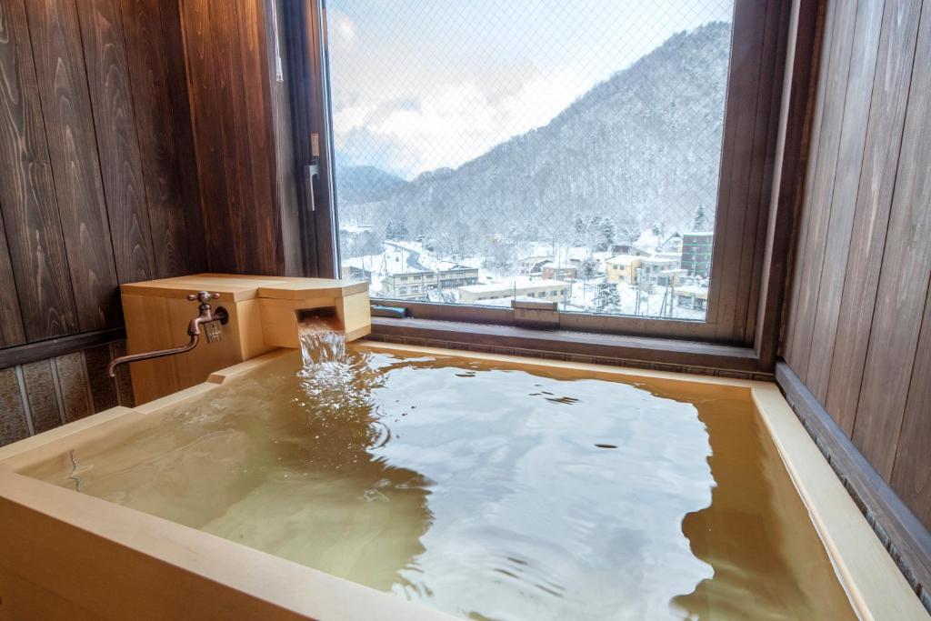 une baignoire dans une pièce avec une grande fenêtre dans l'établissement Jozankei Onsen Yurakusoan, à Jozankei 74 autres photos