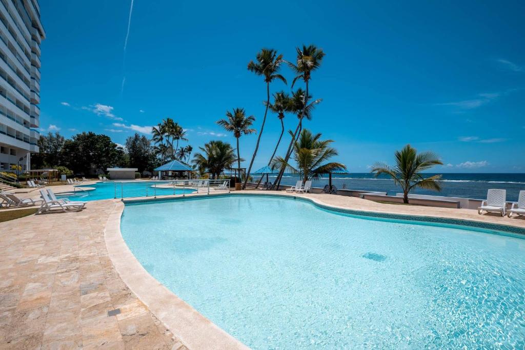 La Puntica de Juan Dolio的住宿－Escape To Paradise Beachfront 2br beach，一座棕榈树和海洋的大型游泳池