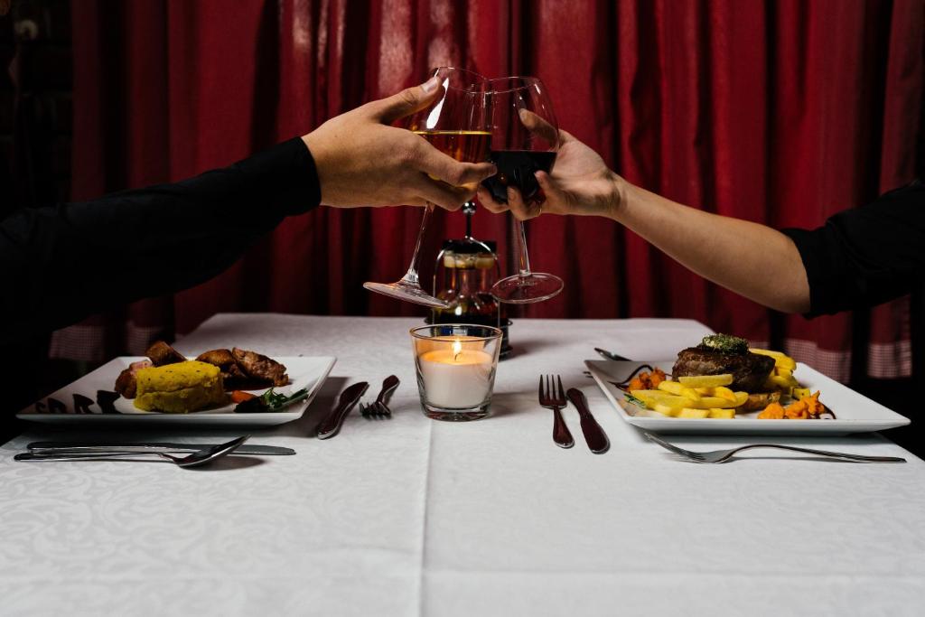 dos personas sosteniendo copas de vino en una mesa con comida en Hotel Picok en Ðurđevac