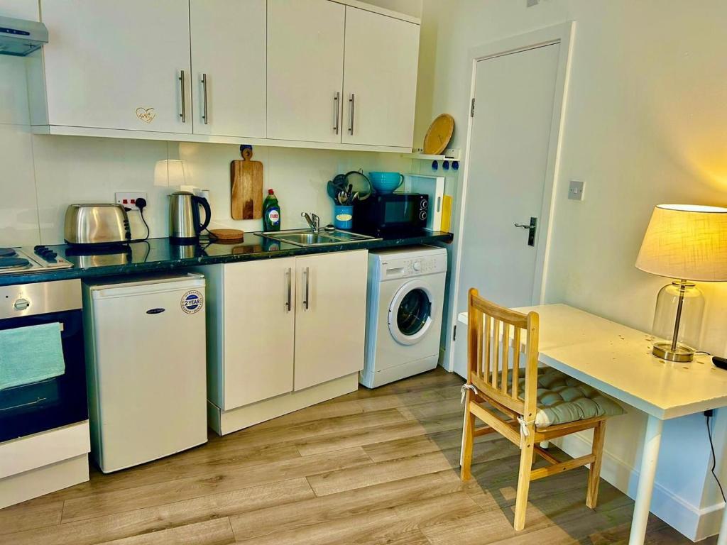 a kitchen with white cabinets and a table with a chair at Studio 5 mins walk from Seven Sisters Station in London
