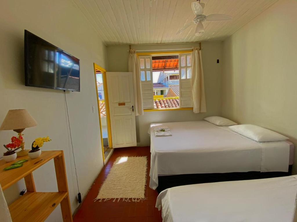 a bedroom with two beds and a tv and a window at Pousada do beco in Caravelas