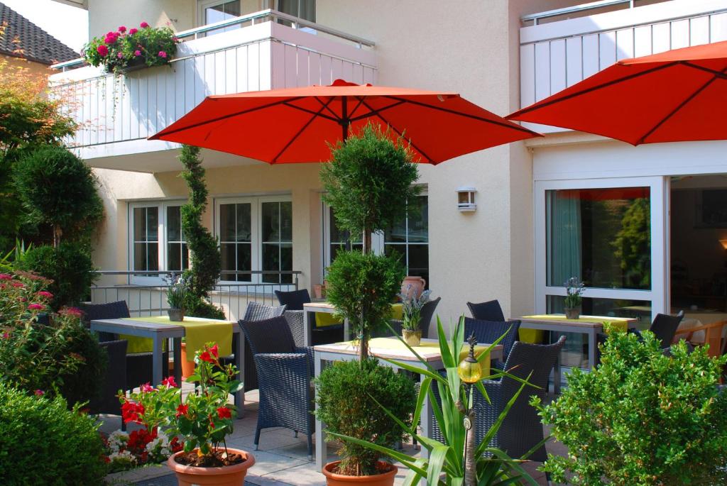 eine Terrasse mit Tischen, Stühlen und roten Sonnenschirmen in der Unterkunft Hotel Im Winkel Appartements und Zimmer in Langenargen