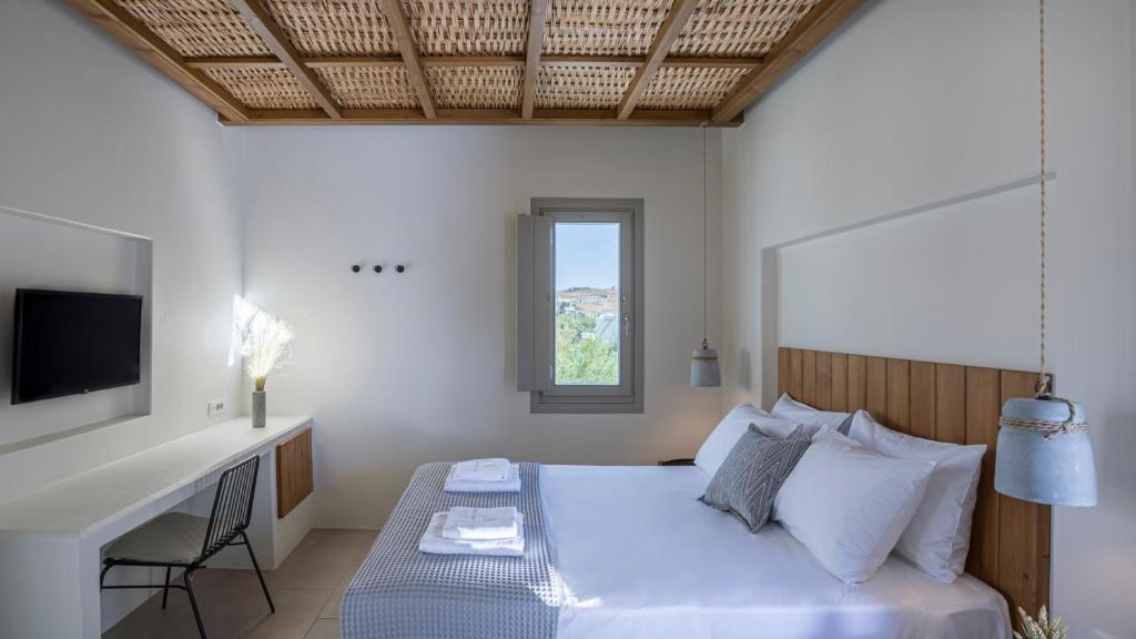 a bedroom with a bed with a desk and a television at Kalami Suites in Livadi