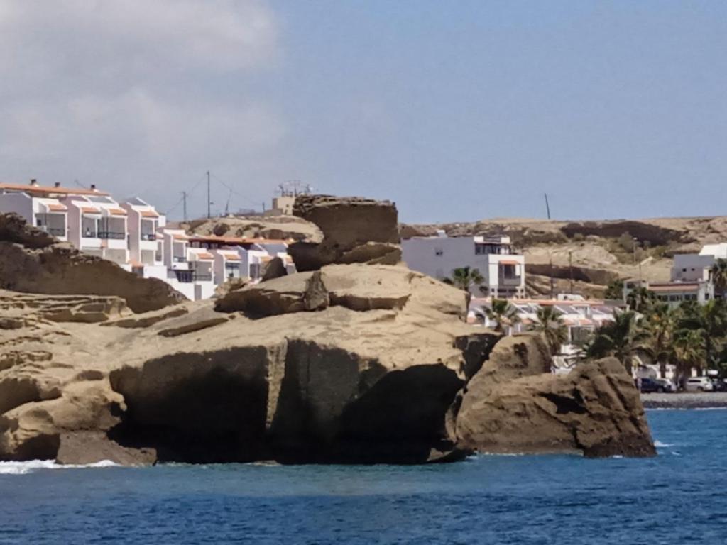a group of rocks in the water with buildings at Arenas del mar in La Mareta