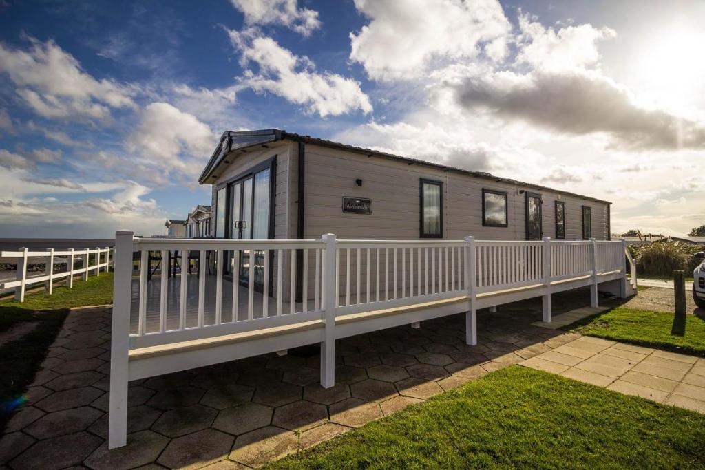 a tiny house with a white fence next to the beach at Beautiful Caravan With Stunning Sea Views At Haven Hopton Ref 80001h in Great Yarmouth