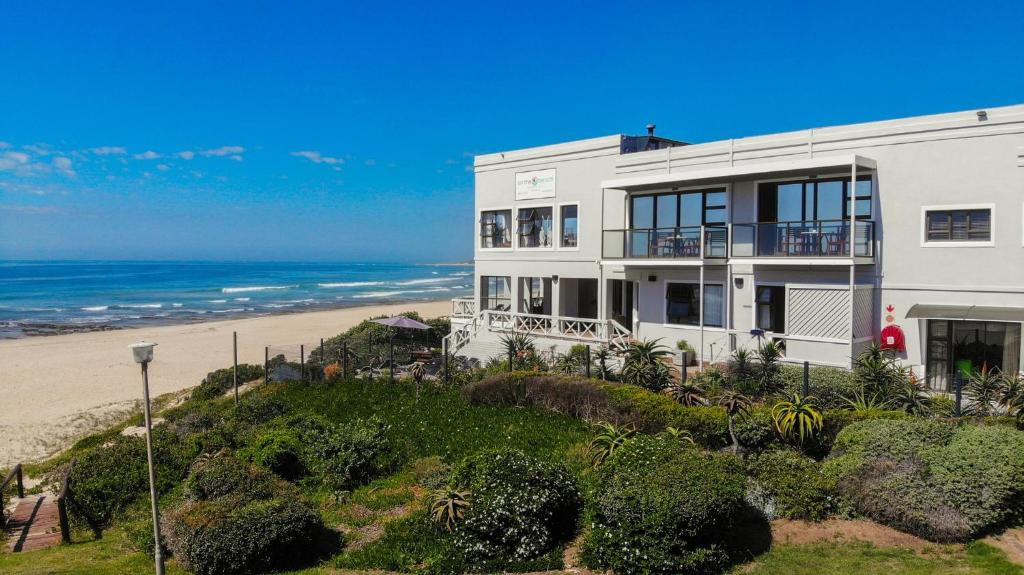 a white house on a hill next to the beach at On the Beach Guesthouse Jeffreys Bay in Jeffreys Bay