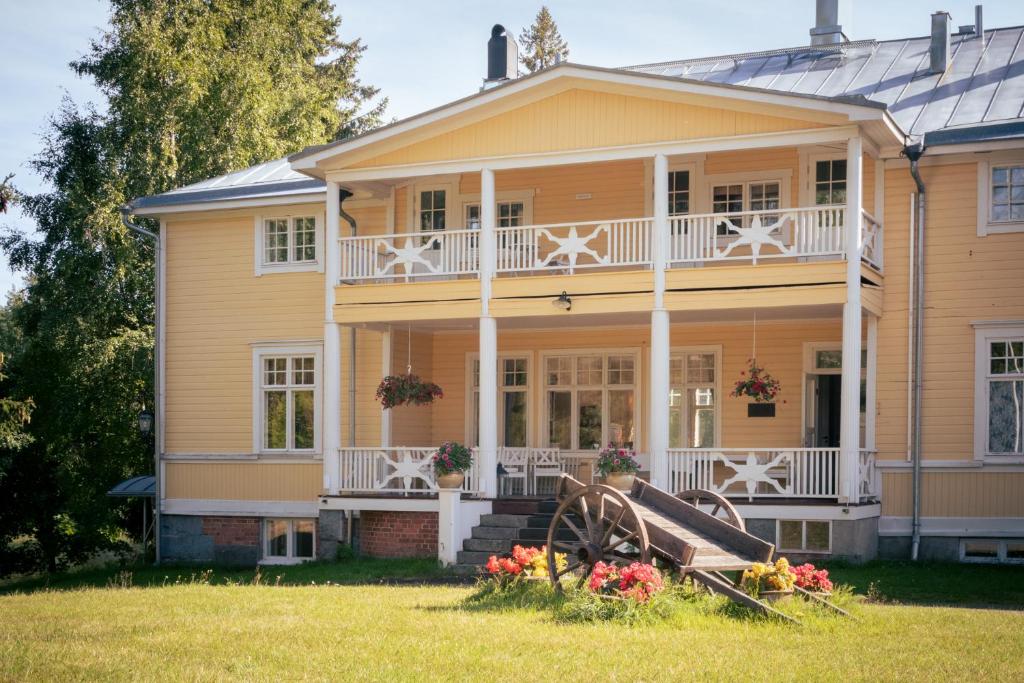 a yellow house with a porch and flowers on the lawn at Landhaus Kekkola in Mikkeli