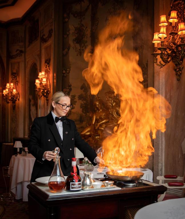 a man in a tuxedo is cooking in front of a fire at The Ritz London in London