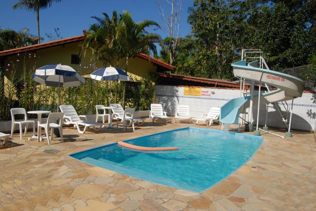 - une piscine avec un toboggan, des chaises et un parasol dans l'établissement Pousada Porto Aventura -Chalés da Luci, à Peruíbe