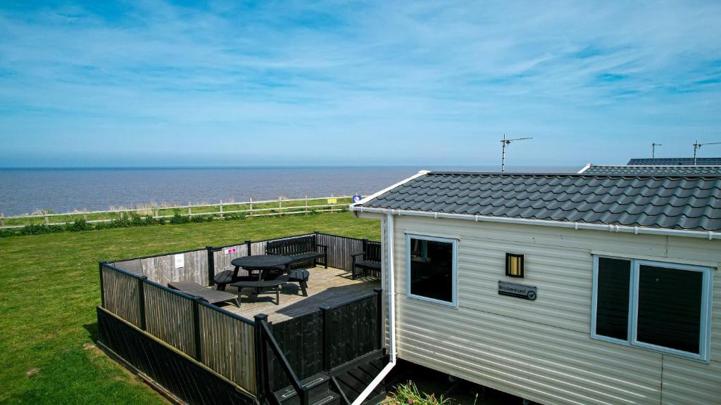 a house with a deck with a picnic table and the ocean at 8 Berth Luxury Caravan With A Full Sea View In Suffolk Ref 20276bs in Hopton on Sea