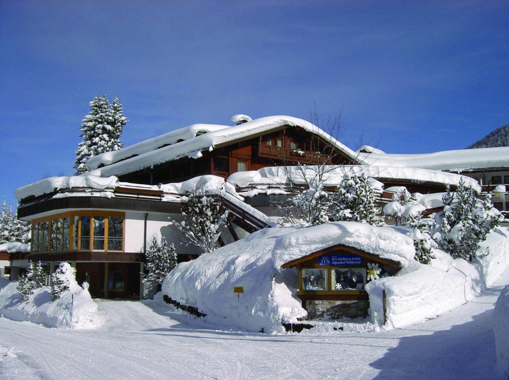 een gebouw bedekt met sneeuw en met sneeuw bedekte bomen bij IFA Alpenhof Wildental Hotel Kleinwalsertal Adults only in Mittelberg