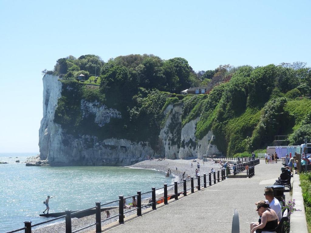 a beach with people sitting on benches next to the water at 2 Bed Chalet St Margaret's at Cliffe South Coast in Dover