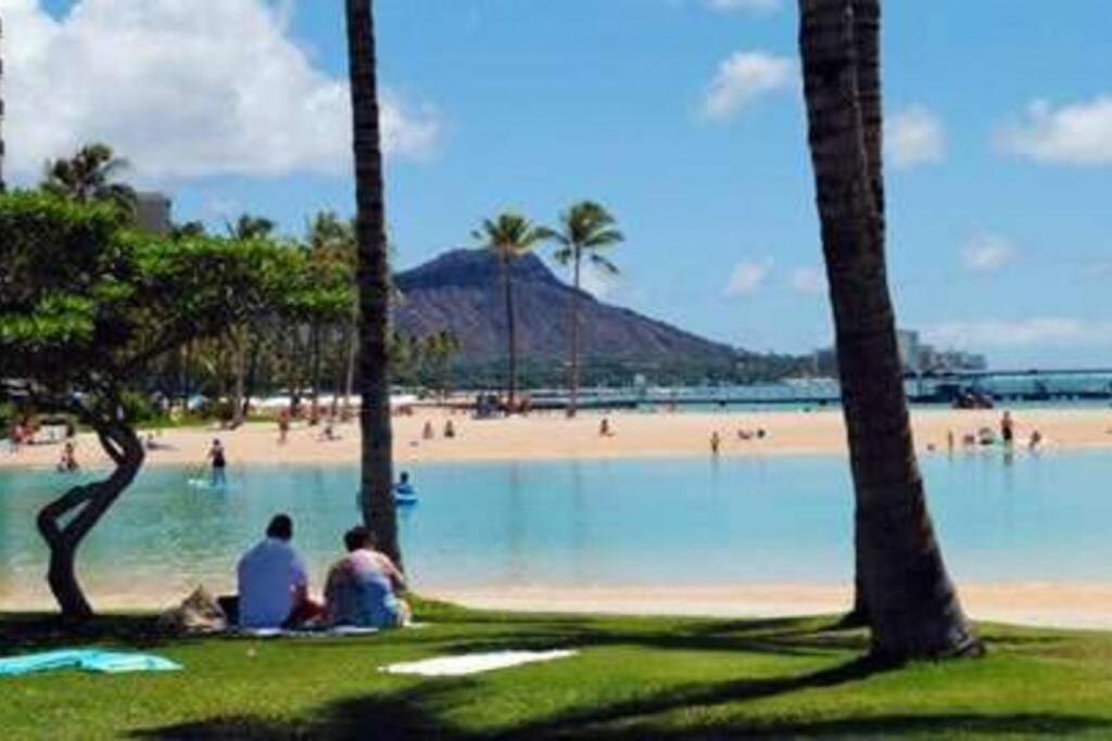 two people sitting next to a beach with palm trees at Ocean Front Amazing One bedroom condo in Honolulu