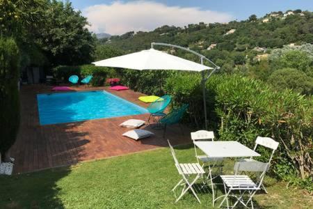 une piscine avec une table, des chaises et un parasol dans l'établissement SAINT PAUL EN JARDIN, à Saint-Paul-de-Vence