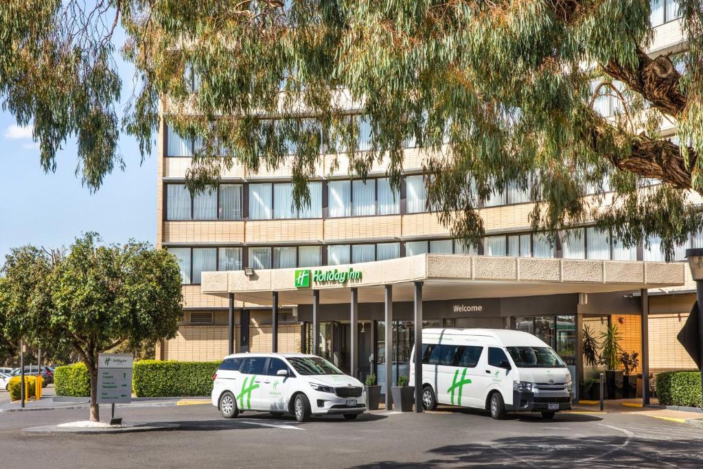 two white vehicles parked in front of a building at Holiday Inn Melbourne Airport, an IHG Hotel in Melbourne